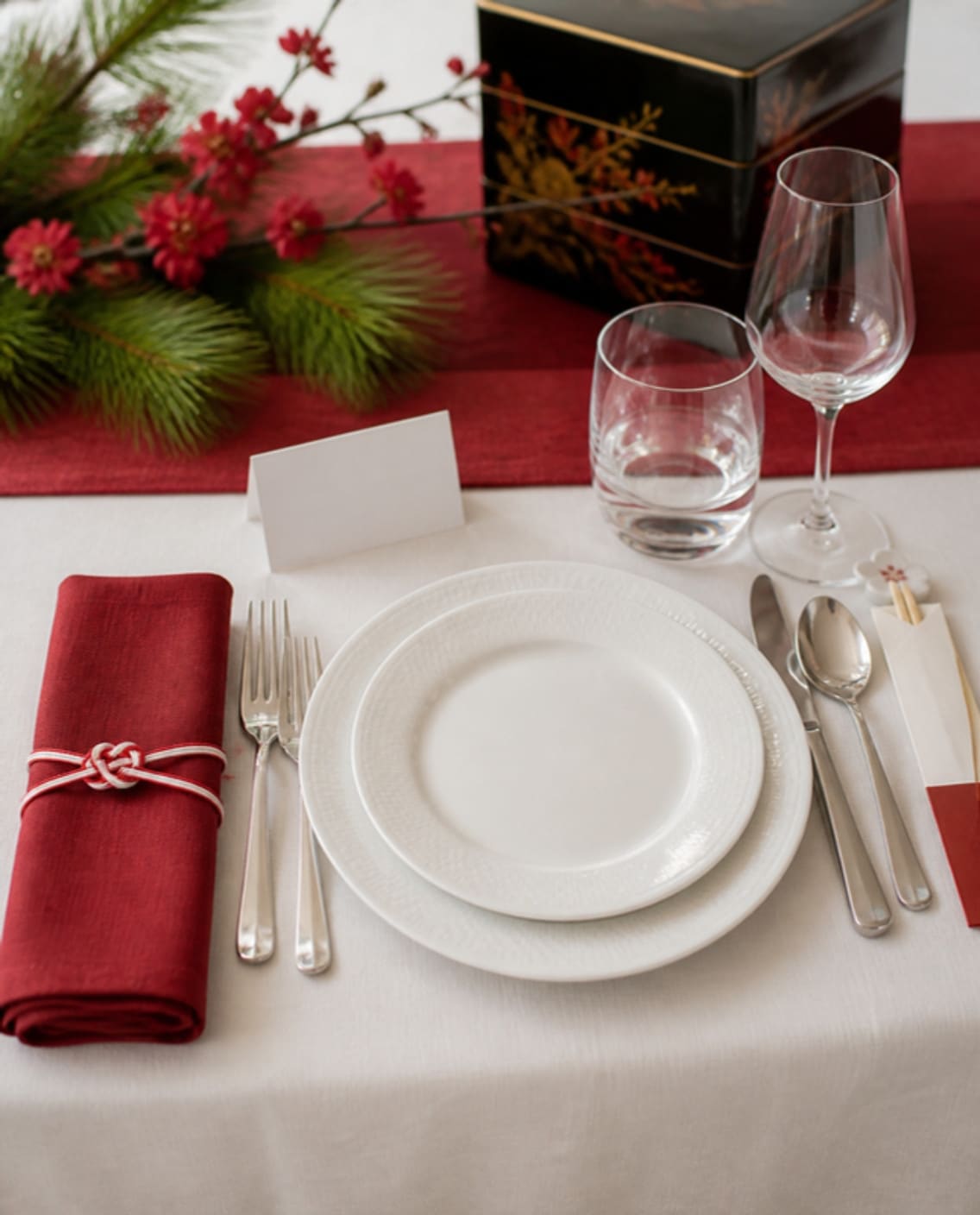 Mood board: Mood board of one place setting: a red napkin tied with red and white cord beside white plates, with chopsticks on a plum blossom rest.